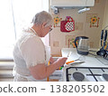 An elderly woman wearing glasses and an apron is busy preparing food in a bright kitchen. 138205502