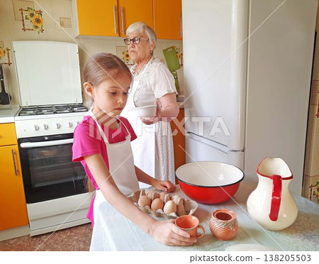 A grandmother and her granddaughter set out the necessary ingredients for cooking on the table. A grandmother and her granddaughter set out the necessary ingredients for cooking on the table. 138205503