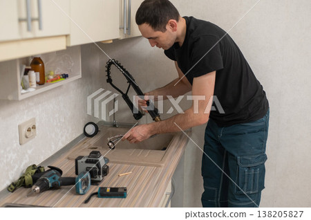 A plumber is replacing a faucet in the kitchen. 138205827