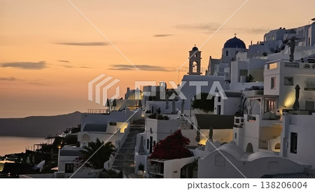 Whitewashed hillside village with blue-domed church overlooking the sea at sunset. 138206004