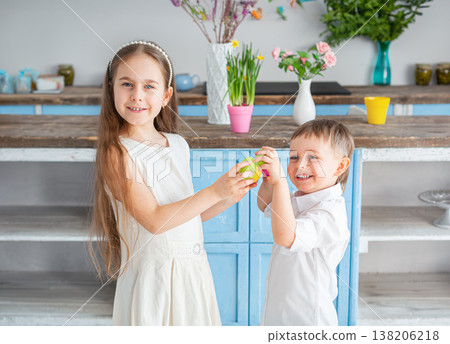 Two smiling children holding green Easter egg together in bright kitchen Two smiling children holding green Easter egg together in bright kitchen 138206218