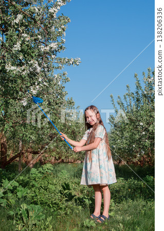 Little girl holding butterfly net standing in blooming orchard with blue sky and fresh green grass Little girl holding butterfly net standing in blooming orchard with blue sky and fresh green grass 138206336