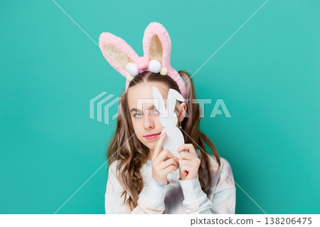 Teenage girl with bunny ears holding wooden bunny toys smiling on bright green background studio 138206475