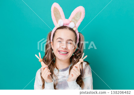 Teenage girl with bunny ears holding wooden bunny toys smiling on bright green background studio 138206482