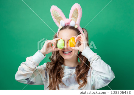 Teenage girl with bunny ears holding pastel Easter eggs in egg holder on green studio background Teenage girl with bunny ears holding pastel Easter eggs in egg holder on green studio background 138206488