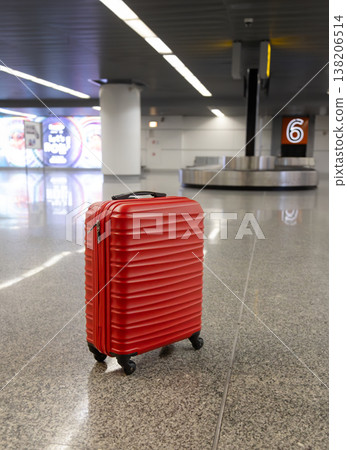 Red suitcase standing on airport baggage claim area near carousel Red suitcase standing on airport baggage claim area near carousel 138206514