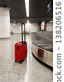 Red suitcase standing on airport baggage claim area near carousel with number sign modern terminal interior. 138206516