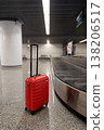 Red suitcase standing on airport baggage claim area near carousel  138206517
