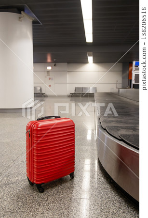 Red suitcase standing on airport baggage claim area near carousel Red suitcase standing on airport baggage claim area near carousel 138206518
