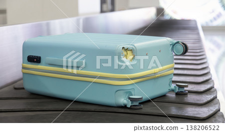 Damaged hard shell suitcase with hole and visible interior on baggage conveyor belt airport close up view. Damaged hard shell suitcase with hole and visible interior on baggage conveyor belt airport close up view. 138206522