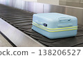 Light blue suitcase moving on airport baggage carousel with metal conveyor system terminal interior. 138206527