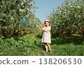 Little girl holding butterfly net standing in blooming orchard with blue sky and fresh green grass 138206530