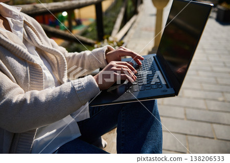 Woman Working Remotely on Laptop While Sitting on Outdoor Bench in Sunny Urban Park 138206533