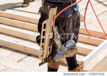Worker stands on construction floor with nail gun in hand, preparing to begin next task on site. Worker stands on construction floor with nail gun in hand, preparing to begin next task on site. 138207430
