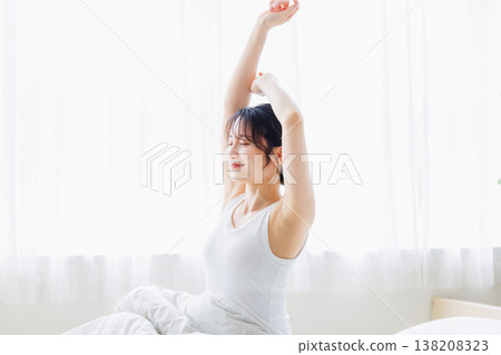 A young woman stretching in her bedroom in the morning. A young woman stretching in her bedroom in the morning. 138208323