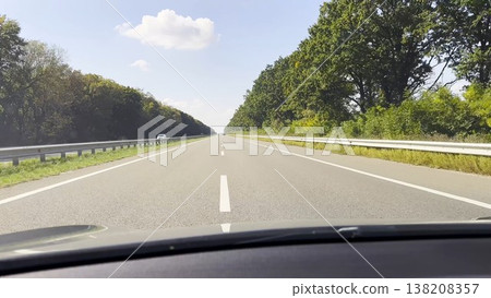 POV from moving car at sunny summer day. Through the windshield white lane marking runs steadily along asphalt road, creating a clear sense of speed, rhythm and open daytime travel POV from moving car at sunny summer day. Through the windshield white lane marking runs steadily along asphalt road, creating a clear sense of speed, rhythm and open daytime travel 138208357