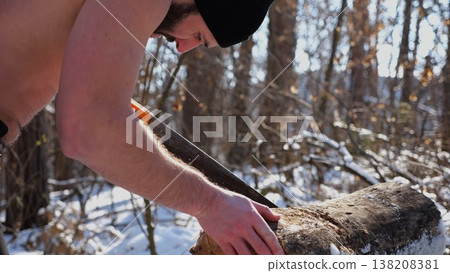 Shirtless bearded man sawing a log in sunny winter forest. Strong guy working with saw in snowy woodland. The scene highlights human effort and outdoor activity in cold conditions. Slow motion Shirtless bearded man sawing a log in sunny winter forest. Strong guy working with saw in snowy woodland. The scene highlights human effort and outdoor activity in cold conditions. Slow motion 138208381