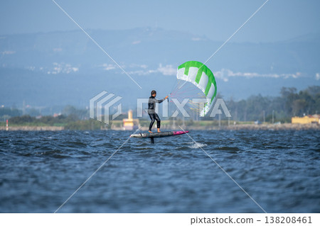 A middle-aged man in a wetsuit glides on a hydrofoil board with a green and white kite A middle-aged man in a wetsuit glides on a hydrofoil board with a green and white kite 138208461