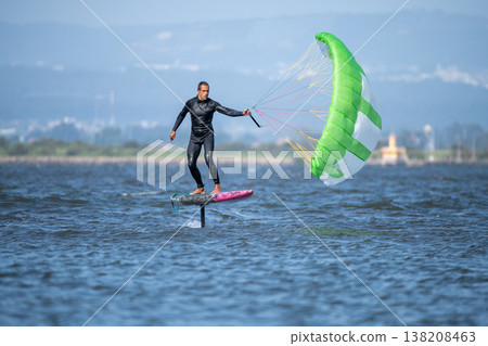 A middle-aged man in a wetsuit glides on a hydrofoil board with a green and white kite 138208463
