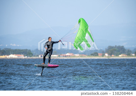 A middle-aged man in a wetsuit glides on a hydrofoil board with a green and white kite A middle-aged man in a wetsuit glides on a hydrofoil board with a green and white kite 138208464