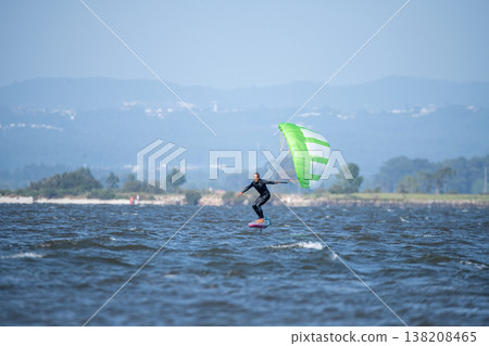A middle-aged man in a wetsuit glides on a hydrofoil board with a green and white kite 138208465