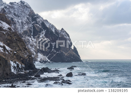 Kabuto-iwa Rock on Raiden Coast in Hokkaido during winter. A landscape of snow-covered cliffs and crashing waves. Kabuto-iwa Rock on Raiden Coast in Hokkaido during winter. A landscape of snow-covered cliffs and crashing waves. 138209195