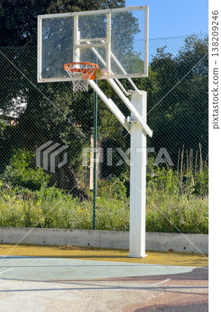 A white basketball hoop and clear backboard with an orange rim stand on an outdoor court A white basketball hoop and clear backboard with an orange rim stand on an outdoor court 138209246