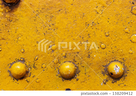 Close up of a yellow painted metal surface with rust, dirt, and round bolt heads. industrial grunge texture background with weathered paint and corrosion. 138209412