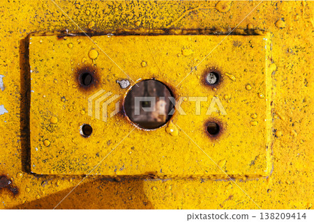 Yellow painted metal plate with a central screw hole and rust stains, showing weathered industrial surface texture. grunge background 138209414