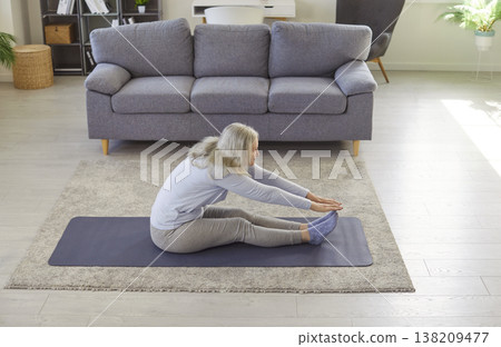 Senior woman stretching on yoga mat, doing seated forward bend to improve flexibility and balance. 138209477