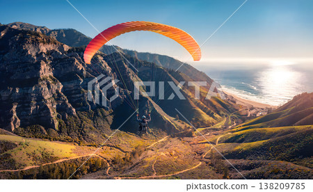 Paraglider soaring over mountain cliffs and a sunny coastline 138209785