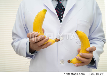 Male doctor stands holding a banana, penis health. Male doctor stands holding a banana, penis health. 138210395