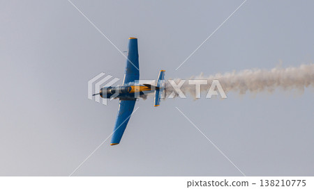 Aircraft performing an aerobatic maneuver with a smoke trail against a clear sky during an aerial aviation display Aircraft performing an aerobatic maneuver with a smoke trail against a clear sky during an aerial aviation display 138210775