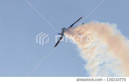Aerobatic propeller airplane performing a steep maneuver while releasing a trail of smoke across a clear blue sky. 138210778