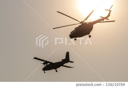 Silhouette of a helicopter and a small airplane flying in formation against a glowing sun 138210784