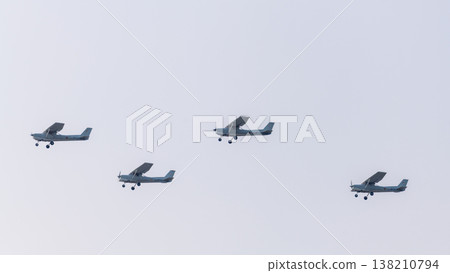 Four light propeller aircraft fly in a coordinated aerial formation against a clear sky during an aviation display at an air show Four light propeller aircraft fly in a coordinated aerial formation against a clear sky during an aviation display at an air show 138210794