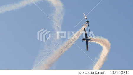 Two aircraft performing aerobatic maneuvers with smoke trails against a clear sky during an aerial aviation display 138210811
