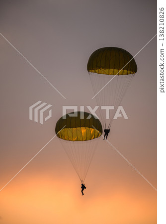 Two combat paratroopers deploying by parachute during an air show demonstration. Silhouettes of troopers descending with glowing parachute canopies against a sunset sky Two combat paratroopers deploying by parachute during an air show demonstration. Silhouettes of troopers descending with glowing parachute canopies against a sunset sky 138210826