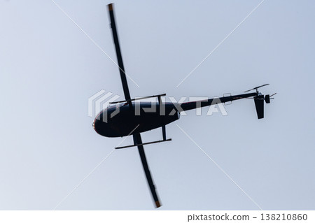 Helicopter flying overhead with spinning rotor blades silhouetted against a clear sky Helicopter flying overhead with spinning rotor blades silhouetted against a clear sky 138210860