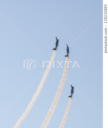 Three aerobatic aircraft performing a synchronized aerial maneuver with curved smoke trails against a clear blue sky during an aviation airshow. Dynamic formation display in an open sky background 138210865
