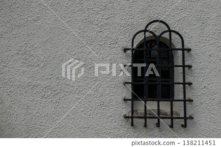 Small arched window with metal grille on textured wall Small arched window with metal grille on textured wall 138211451