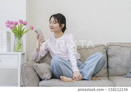 A young woman sitting on a sofa looking at her smartphone 138212236