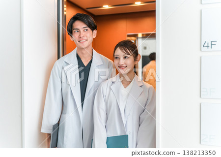 一名身穿白大褂的男醫生和一名身穿白大褂的女醫生正在使用電梯。 一名身穿白大褂的男醫生和一名身穿白大褂的女醫生正在使用電梯。 138213350