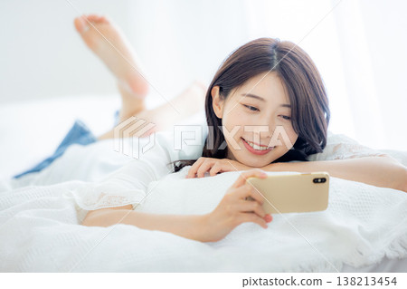 一名婦女在床上的看一個智能手機 138213454