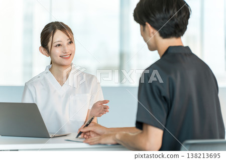 一名身穿護士制服的護士和一名女諮商師正在與一名男病人交談。 138213695