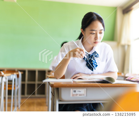 A female student diligently writing in the classroom. 138215095