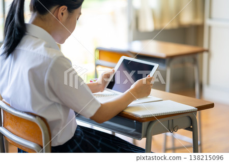 The back view of a female student looking at a tablet in a classroom. 138215096