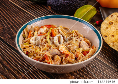 Stir-fried seafood noodles with shrimp and squid in a bowl on a wooden table. 138215616