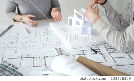 Architects discussing modern building design with 3d model and blueprints during planning meeting focused on innovation, teamwork and sustainable construction solutions, close up 138216309