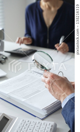 Two professional accountants or auditors reviewing financial reports and analyzing data using a calculator and a magnifying glass. Audit and taxes in business 138216319